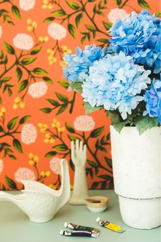 blue flowers are in a white vase on a table next to a bird and wallpaper