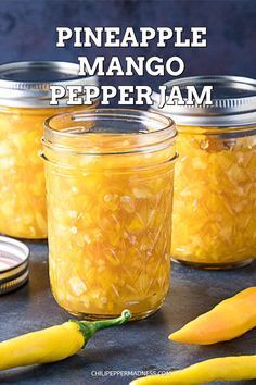 three jars filled with pineapple mango pepper jam on top of a table next to two yellow peppers