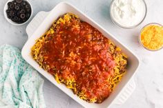 an enchilada casserole in a white dish with sour cream and olives on the side