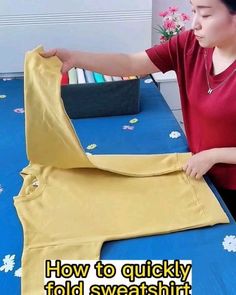 a woman in red shirt holding up a yellow piece of cloth on top of a blue table