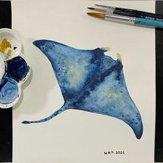 a watercolor painting of a blue stingfish next to some paintbrushes on a table