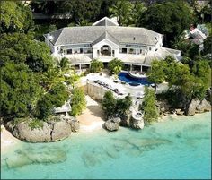 an aerial view of a large house on the beach with trees surrounding it and blue water