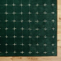 a green rug with white crosses on the top and bottom, sitting on a wooden floor