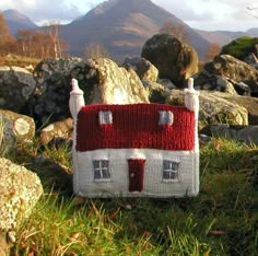 a knitted house sitting on top of a grass covered field next to some rocks