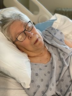 an older woman laying in a hospital bed with her head on the pillow and eyeglasses over her eyes