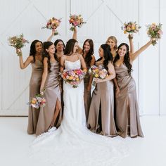 a group of women standing next to each other in front of a barn door holding bouquets