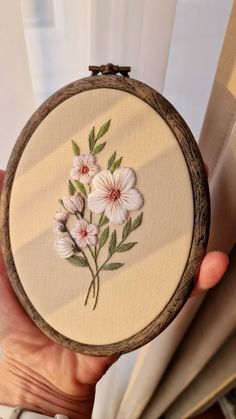 a person holding up a small embroideryed flower in front of a window sill