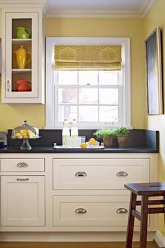 a kitchen with yellow walls and white cupboards, black counter tops and wooden stools