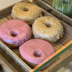 three donuts with pink frosting in a wooden box