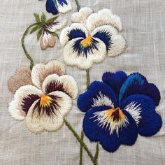 three blue and white pansies on a linen surface with green stems in the center