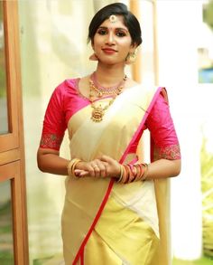 a woman wearing a yellow and pink sari with gold jewelry on her neck, standing in front of a door