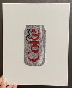 a hand holding up a piece of art with the word coke on it in red and white