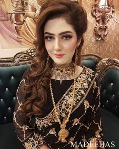 a woman with long hair wearing a black dress and gold jewelry on her head, sitting in