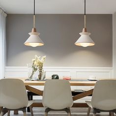 a dining room table with four chairs and two pendant lights hanging over it, in front of a gray wall