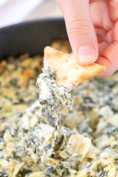 a hand holding a cracker with spinach and cheese on it in a skillet