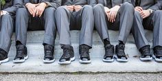 four men in suits and shoes sitting on steps with their legs crossed, all wearing black sneakers