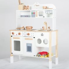 a wooden play kitchen with white appliances and accessories on it's shelves, in front of a gray background