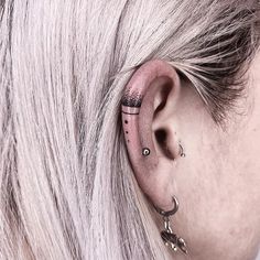 a woman with blonde hair has piercings on her ears and behind her ear is a small cross