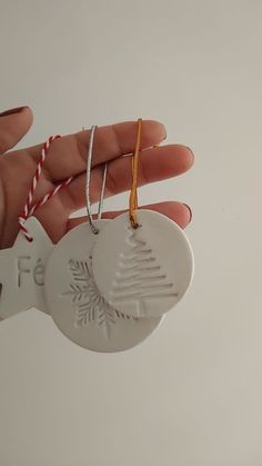 a hand holding a white ceramic ornament with a tree on it's side