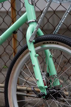 the front wheel of a mint green bicycle parked in front of a chain link fence