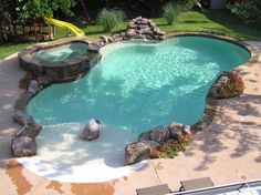 an outdoor swimming pool surrounded by rocks and water features a slide in the back yard