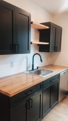 an empty kitchen with black cabinets and wood counter tops