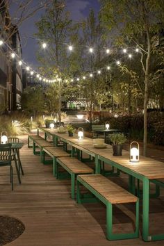 an outdoor dining area with wooden tables and benches lit up by string lights at night