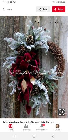 a christmas wreath with pine cones and red velvet bow hanging on a wooden door frame