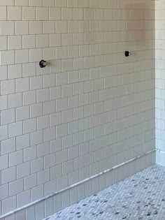 an empty bathroom with white tile and black handles on the shower wall, next to a tiled floor