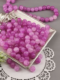 pink beads are in a glass bowl on a doily next to a white flower