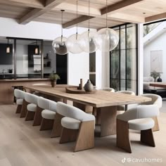 a large wooden table surrounded by white chairs and hanging lights in an open kitchen area