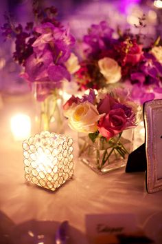 flowers in vases and candles on a table with lights around them at a wedding