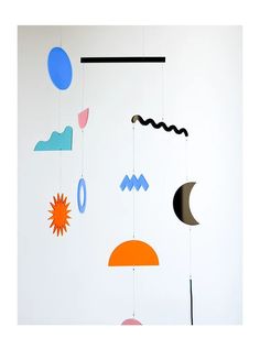 a mobile with various shapes and colors hanging from it's sides on a white wall