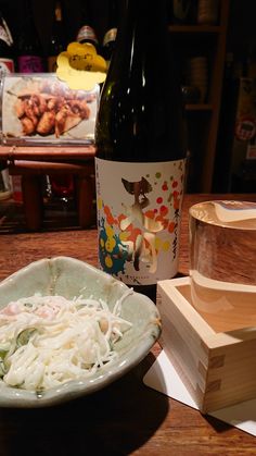 a bowl of noodles next to a bottle of wine on a table with other items