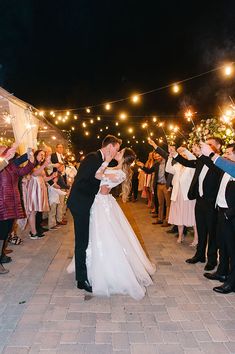 a bride and groom kissing in front of their wedding party with sparklers all around them