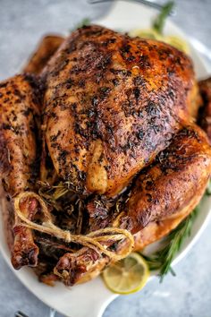 a roasted chicken on a plate with lemons and herbs