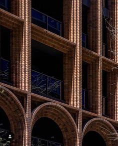 a clock on the side of a brick building with arches and trees in front of it