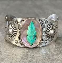 This is an exceptional FRED HARVEY ERA Navajo sterling silver REPOUSSE bracelet. This stunning scalloped bracelet features hand carved turquoise leaf and an oval shaped abalone shell in the center. Deeply stamped Eagle feathers,Head dress, Sun symbols, Sun Rays , Rattlesnake jaws, Horses and arrows. RARE PIECE There is no purity mark ,however it has been tested positive for sterling silver. The inside measurement from tip to tip is approximately 5-7/8" and the opening measurement between the tip is approximately 1-5/8" Approximate width of the bracelet is 2-3/4" (across inside). Approximate size of the abalone shell oval is 1-1/2" L (North to South), 1" (West to East). Sturdy 49.3 grams in my scale. ADJUSTABLE & STACKABLE Bracelet This bracelet fits 6-3/4",7",7-1/4",7-1/2" size wrists. Thi Eagle Feathers, Large Bracelet, Feather Headdress, Southwestern Jewelry, Stackable Bracelets, Abalone Shell, Sterling Silver Cuff, Silver Cuff, Beautiful Bracelet