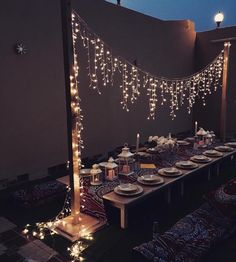 a long table with lights strung from it and plates on the table in front of it