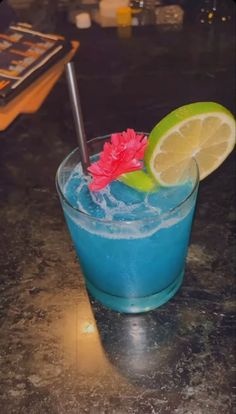 a blue cocktail with lime and a flower on the rim is sitting on a counter