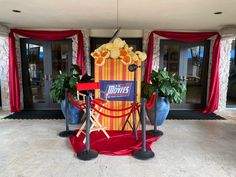 an entrance to a movie theater with red carpet and yellow striped curtained walls, decorated with flowers