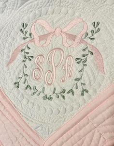 the monogrammed quilt has a pink ribbon on it and is adorned with green leaves