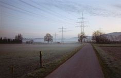 a foggy field with power lines and telephone poles in the distance on a dirt road