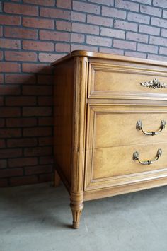 an old wooden dresser sitting in front of a brick wall with two handles on each drawer