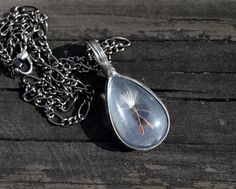 a dandelion seed in a tear hanging from a chain on a wooden surface