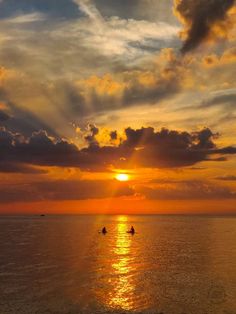 the sun is setting over the ocean with two people on small boats in the water