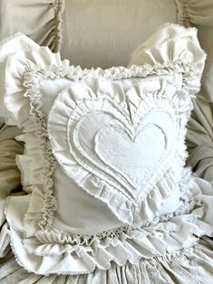 a white heart pillow sitting on top of a bed with ruffled sheets and pillows