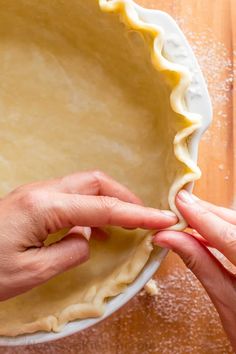 two hands are placing dough into a pie pan