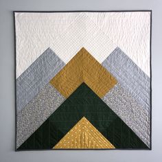 a quilted wall hanging on the side of a gray wall with yellow and green triangles