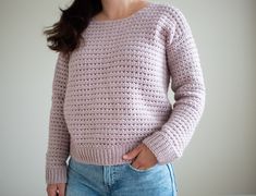 a woman wearing a pink sweater and jeans standing in front of a white wall with her hands on her hips